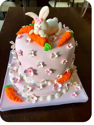 Bolo de 1 andar no tema Páscoa com cores suaves, no topo do bolo uma coelha comendo uma cenoura e cenouras, na base flores por todo o bolo do Curso Meu Primeiro Zoológico - Modele 25 Animais em Pasta Americana