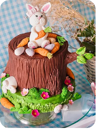 Bolo de 1 andar no tema Páscoa com cores fortes, no topo do bolo o tronco de uma árvore com uma coelha e cenouras e ovos de páscoa espalhados, na base do bolo um coelho entalado no tronco, com um jardim ao redor do Curso Meu Primeiro Zoológico - Modele 25 Animais em Pasta Americana