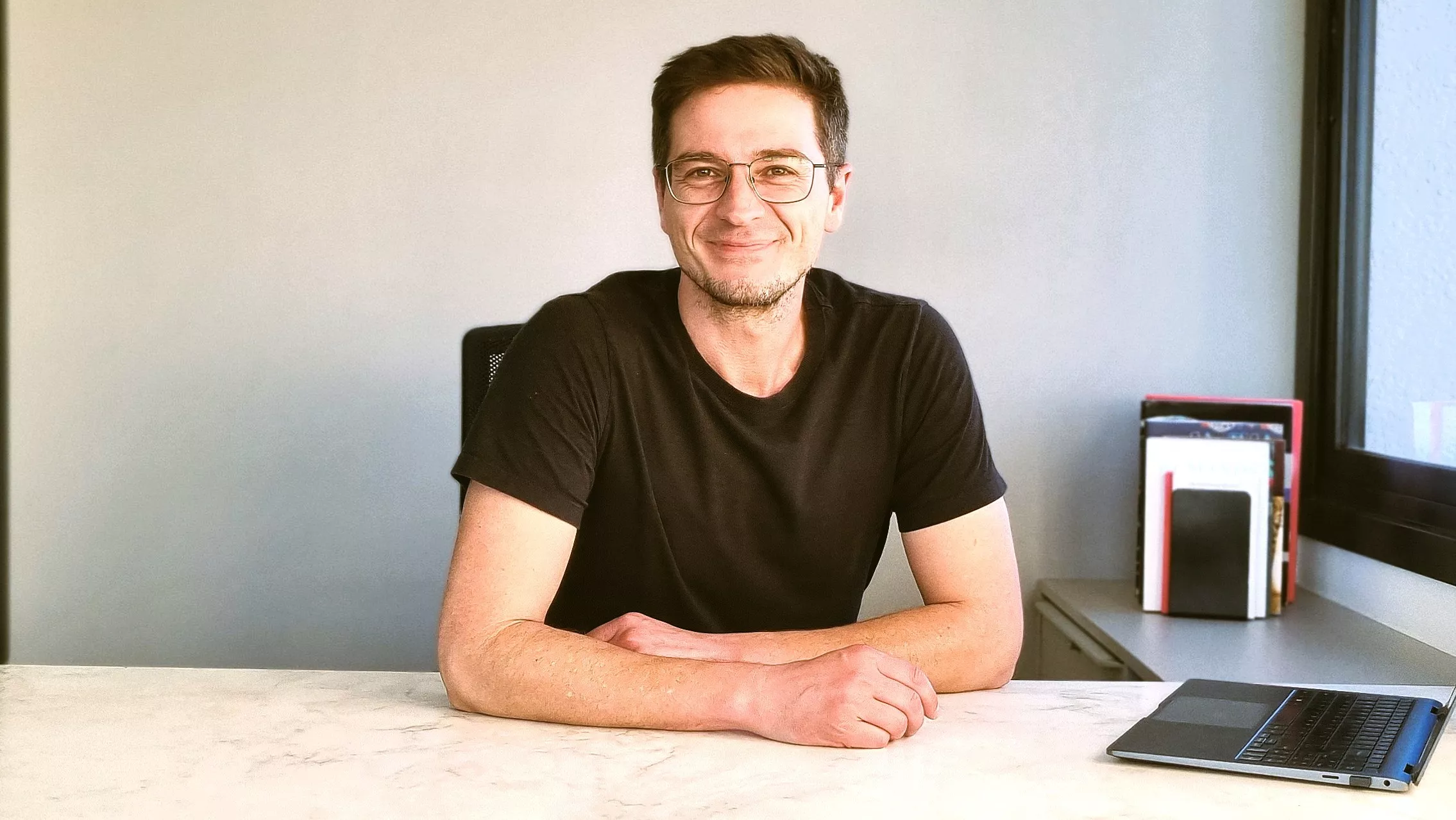 Icaro Bonamigo Gaspodini no centro da imagem, de camistea preta e óculos, com os braços cruzados sobre a mesa. 