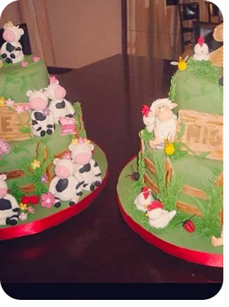Bolos de 2 andares cada para gêmeos, com vaquinhas, galinhas, pintinhos, patinhos ovelhas nos topos e bases do bolo, na base do bolo ainda cerquinhas e flores espalhadas todas num fundo verde representando grama do Curso Meu Primeiro Zoológico - Modele 25 Animais em Pasta Americana