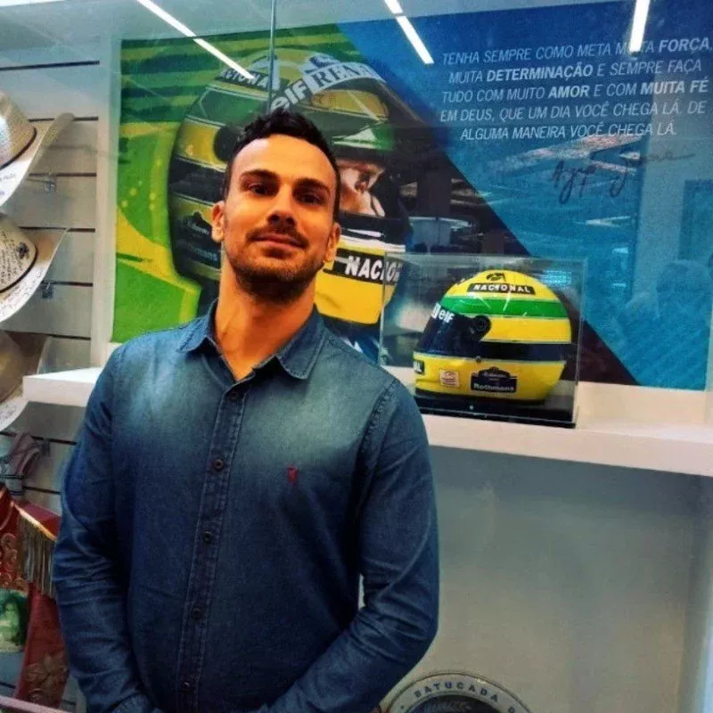 Foto do criador do produto, Elvis Ferreira, ao lado do capacete de Ayrton Senna no Santuário Nacional de Aparecida