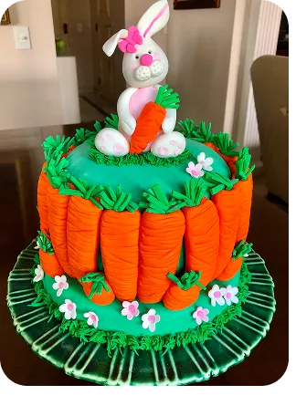 Bolo de 1 andar no tema Páscoa com cores fortes, no topo do bolo uma coelha segurando sua cenoura, na base do bolo cenouras, com um jardim ao redor do Curso Meu Primeiro Zoológico - Modele 25 Animais em Pasta Americana