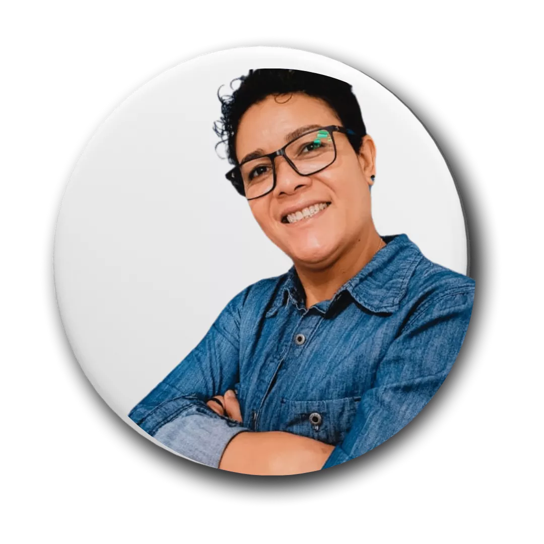 mulher branca, usando oculos de aro preto, uma camisa social azul, braços cruzados e sorrindo